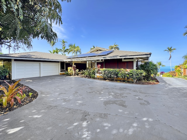 single story home featuring a garage, solar panels, and driveway