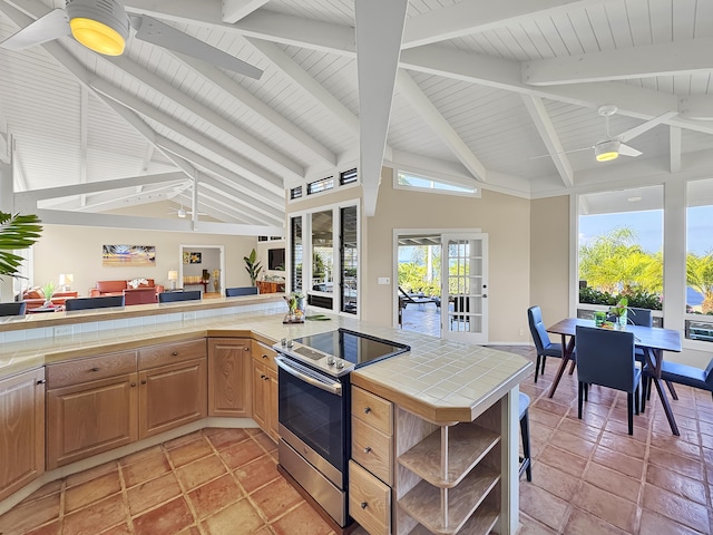 kitchen with vaulted ceiling with beams, stainless steel electric stove, tile countertops, a ceiling fan, and open shelves