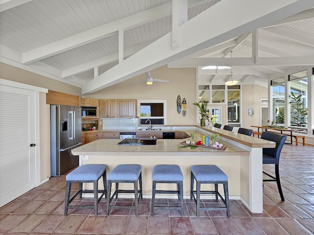 kitchen featuring vaulted ceiling with beams, built in microwave, light countertops, high end refrigerator, and a kitchen breakfast bar