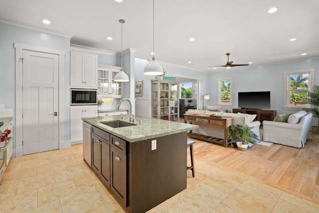 kitchen featuring black microwave, a kitchen island with sink, a sink, white cabinetry, and dishwasher