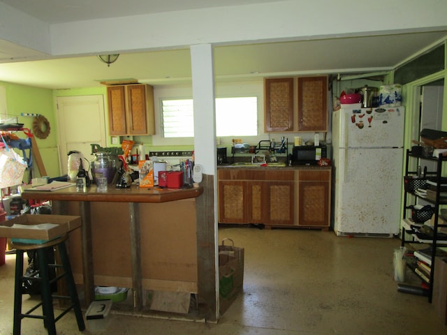 kitchen featuring brown cabinets, dark countertops, freestanding refrigerator, black microwave, and a kitchen breakfast bar