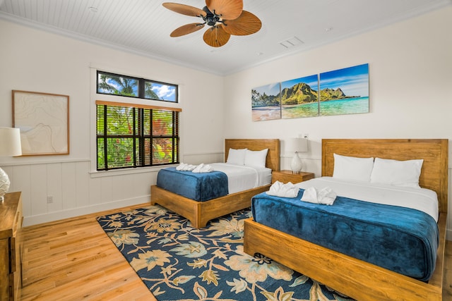 bedroom with wood finished floors, a ceiling fan, visible vents, wainscoting, and crown molding