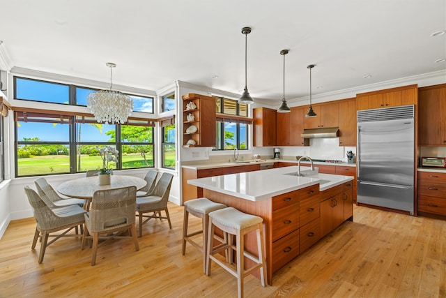 kitchen featuring under cabinet range hood, hanging light fixtures, light countertops, light wood-type flooring, and stainless steel built in fridge