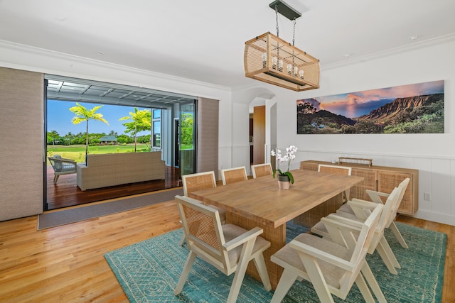 dining area featuring crown molding, arched walkways, wood finished floors, and wainscoting