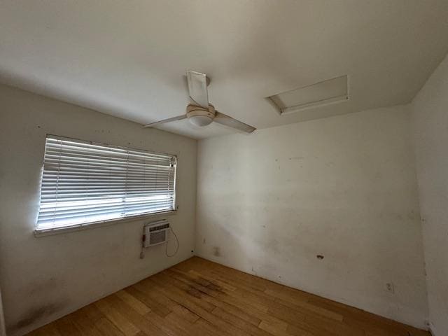 spare room featuring attic access, light wood-type flooring, a ceiling fan, and a wall mounted AC