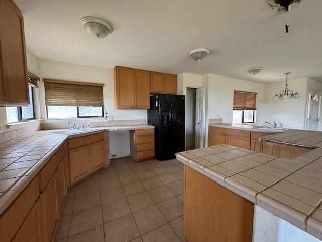 kitchen with decorative light fixtures, light tile patterned floors, tile counters, a sink, and black fridge