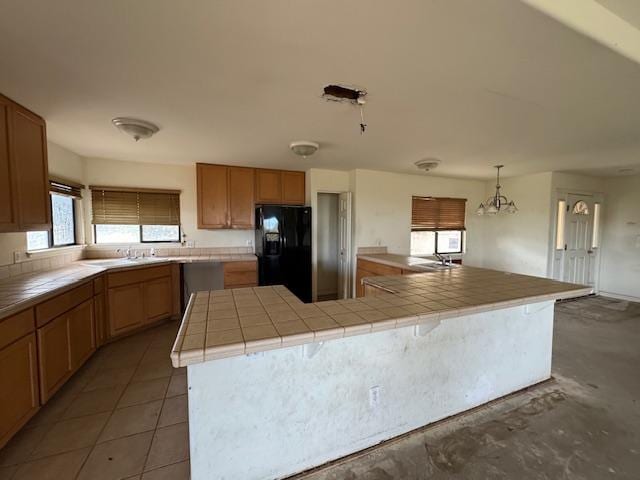 kitchen with hanging light fixtures, tile countertops, black fridge, and a center island