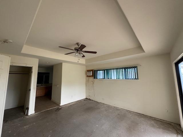 unfurnished bedroom featuring a ceiling fan, a tray ceiling, and concrete flooring