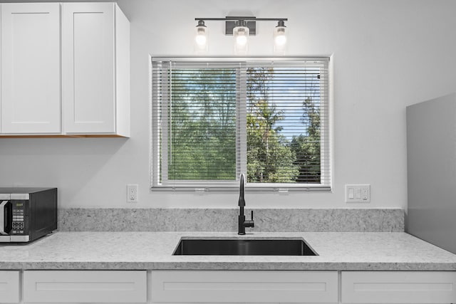 kitchen with white cabinetry, light stone counters, and a sink