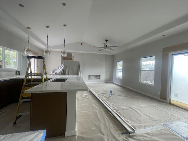 kitchen with light stone counters, baseboards, a kitchen island with sink, vaulted ceiling, and decorative light fixtures