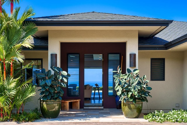 doorway to property featuring roof with shingles and stucco siding