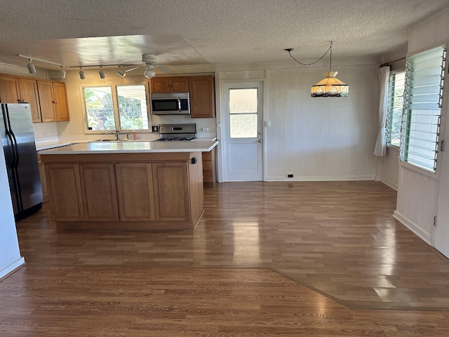 kitchen with stainless steel appliances, light countertops, brown cabinetry, dark wood-type flooring, and a textured ceiling