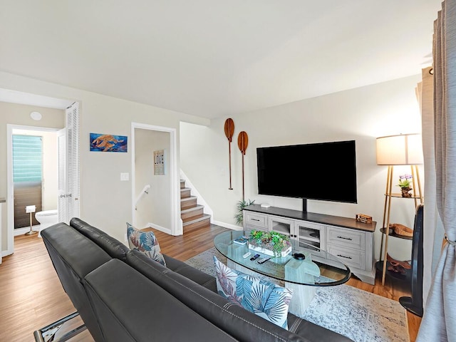 living room featuring light wood-type flooring, baseboards, and stairs