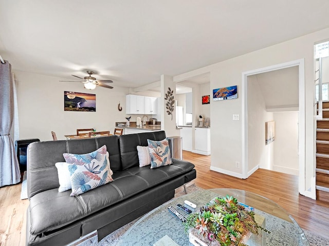 living area featuring light wood-style flooring, baseboards, stairs, and ceiling fan