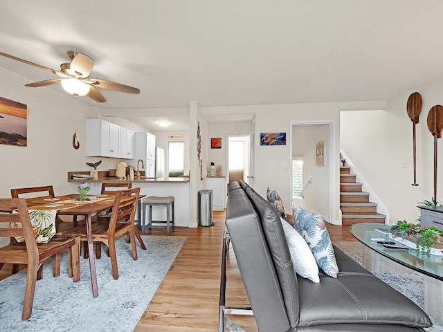 dining area with ceiling fan, light wood-style flooring, and stairs