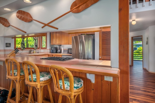 kitchen featuring tile counters, a breakfast bar, wood finished floors, freestanding refrigerator, and gas cooktop