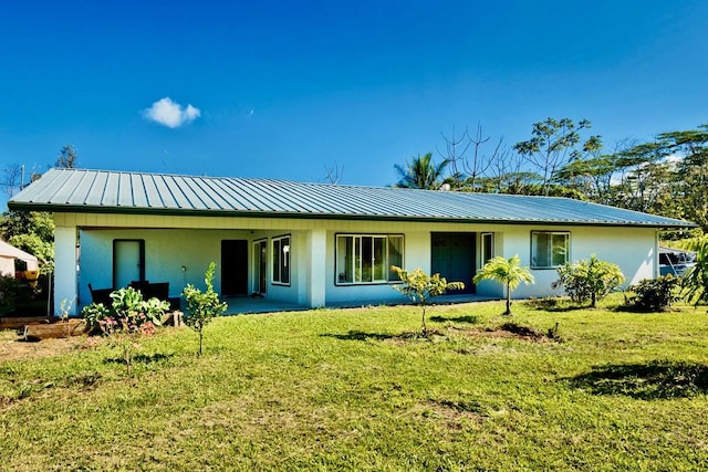 rear view of property featuring a yard, metal roof, and stucco siding