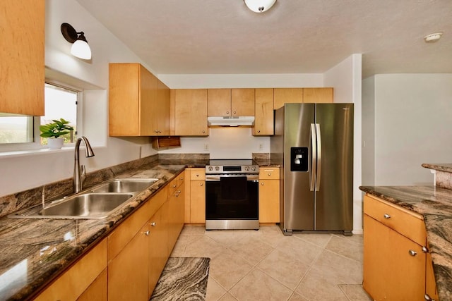 kitchen with light tile patterned floors, dark stone countertops, stainless steel appliances, under cabinet range hood, and a sink