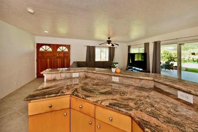 kitchen featuring light tile patterned floors, a textured ceiling, stone countertops, a ceiling fan, and open floor plan