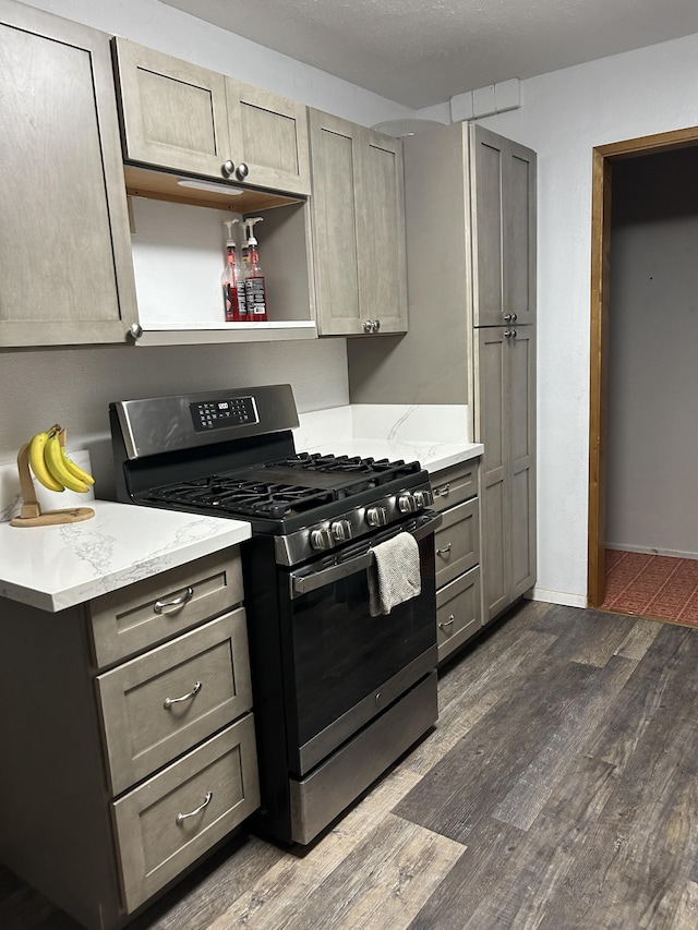 kitchen with baseboards, gas stove, dark wood finished floors, and light stone countertops