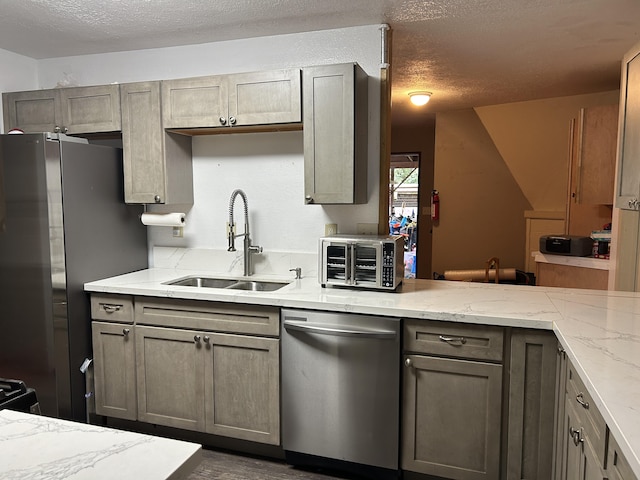 kitchen featuring light stone counters, gray cabinets, appliances with stainless steel finishes, a sink, and a textured ceiling