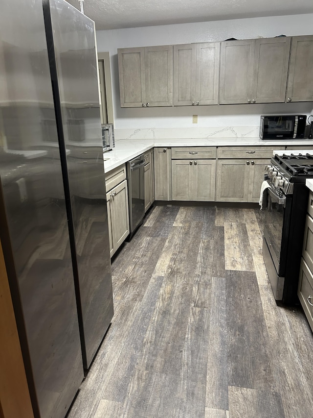 kitchen with a textured ceiling, light stone counters, gray cabinetry, stainless steel appliances, and dark wood finished floors