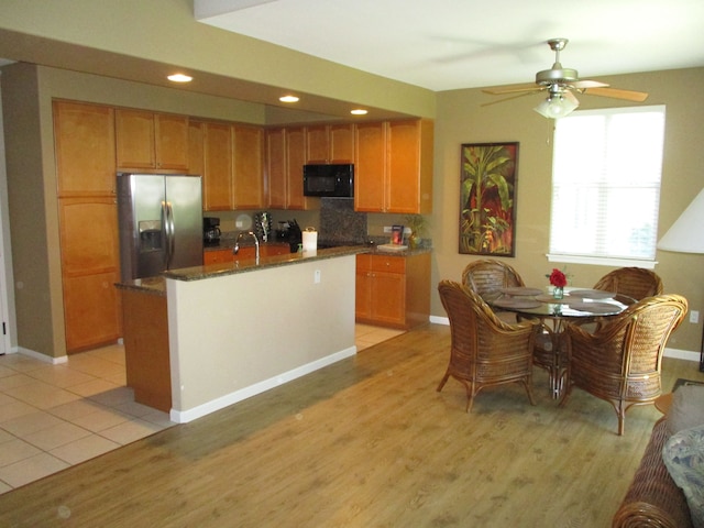 kitchen with black microwave, a kitchen island with sink, stainless steel refrigerator with ice dispenser, and light wood-style flooring