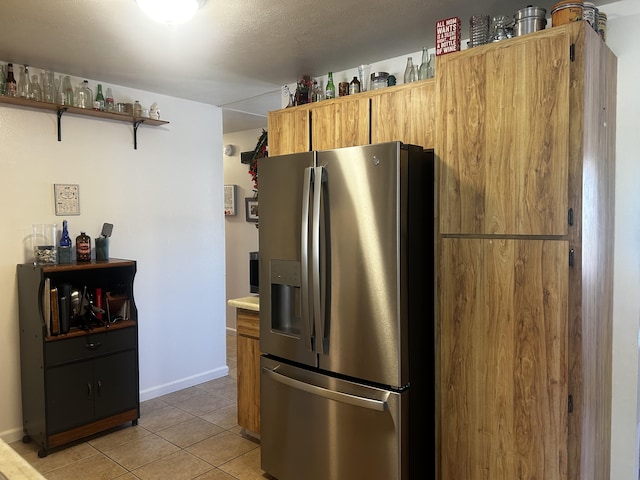 kitchen featuring light tile patterned floors, baseboards, light countertops, stainless steel fridge with ice dispenser, and open shelves