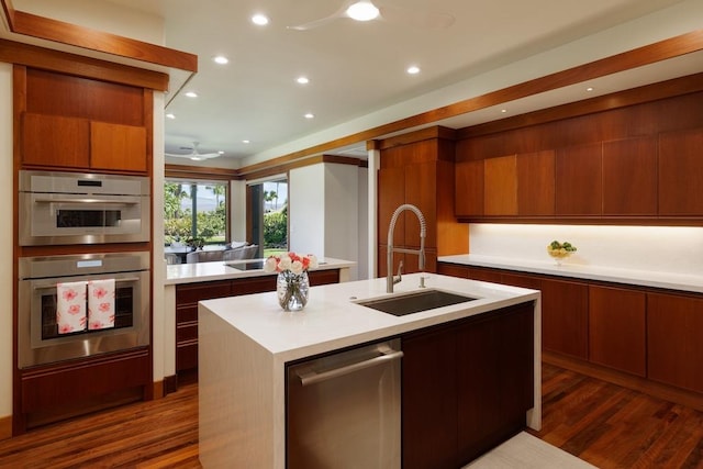 kitchen featuring light countertops, double oven, a kitchen island with sink, a sink, and modern cabinets