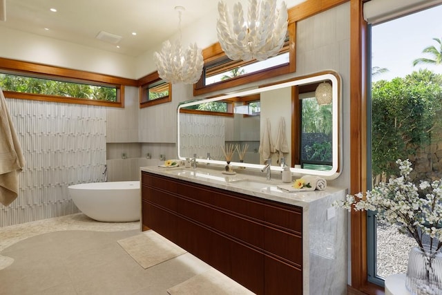 bathroom with tile patterned flooring, a soaking tub, double vanity, and an inviting chandelier