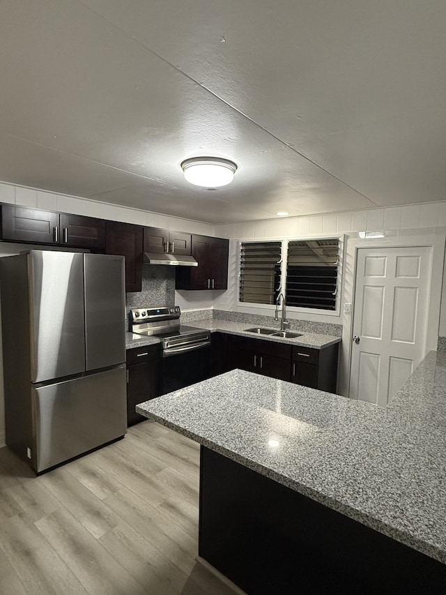 kitchen featuring a sink, light stone counters, under cabinet range hood, light wood-style floors, and appliances with stainless steel finishes