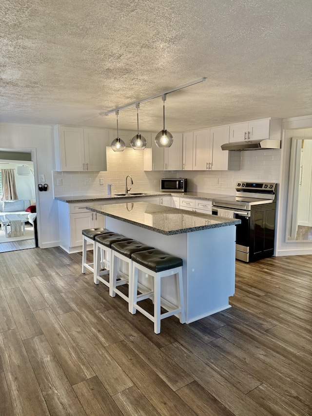 kitchen featuring dark wood-type flooring, under cabinet range hood, appliances with stainless steel finishes, white cabinetry, and a center island