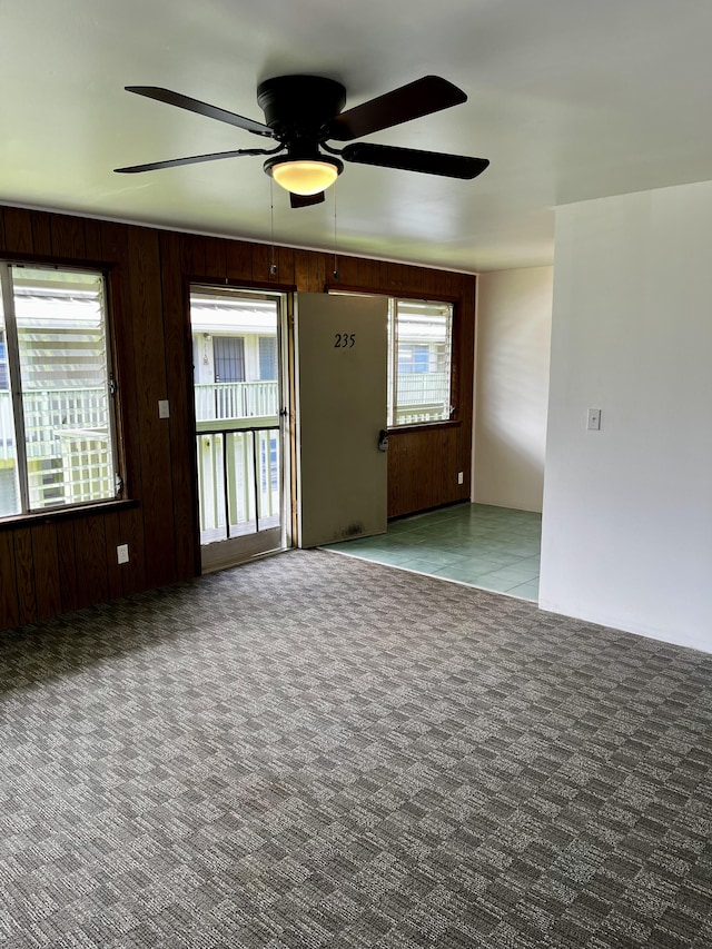 spare room featuring carpet floors, ceiling fan, and wooden walls