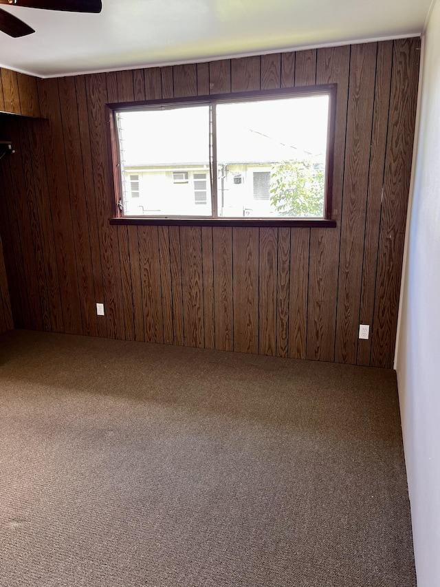 unfurnished room with carpet floors, a ceiling fan, and wooden walls