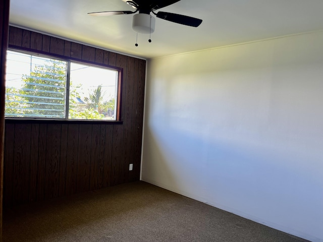 empty room featuring a ceiling fan, carpet, and wooden walls