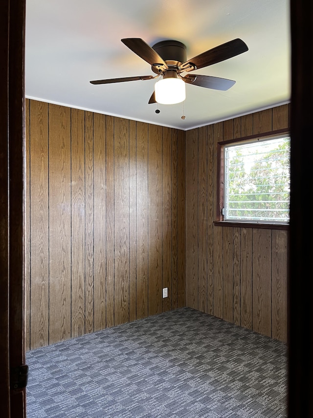 carpeted spare room with ceiling fan and wood walls