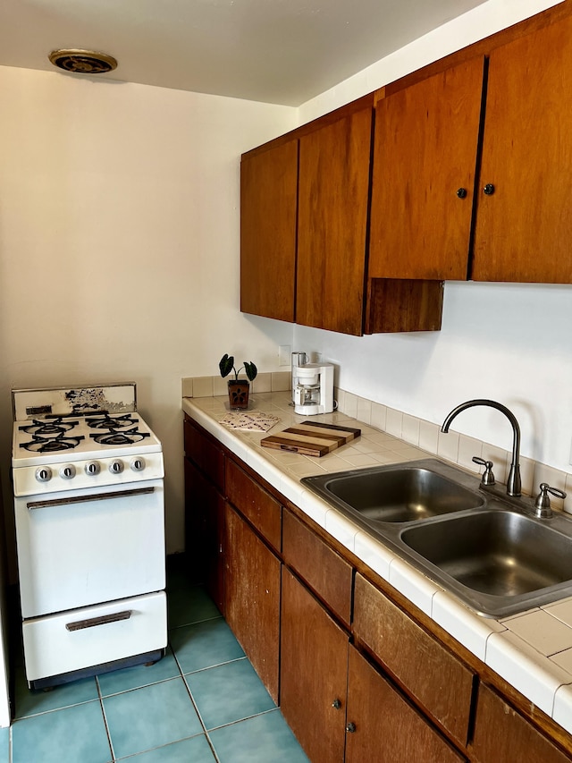 kitchen featuring a sink, tile patterned flooring, tile counters, and gas range gas stove