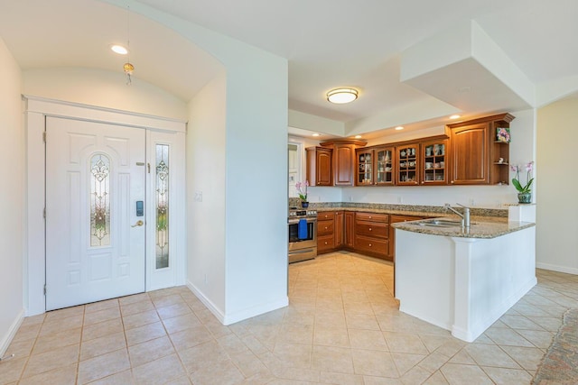 kitchen featuring stone countertops, brown cabinetry, a peninsula, stainless steel range with electric stovetop, and a sink