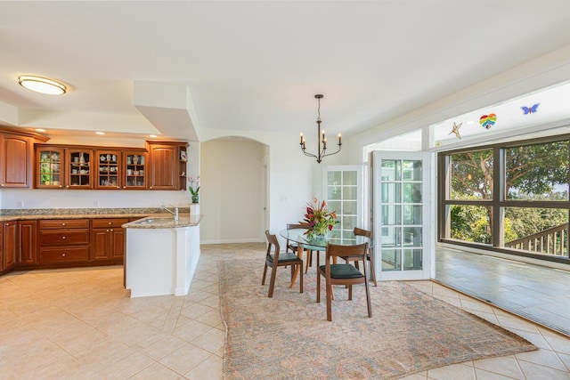 kitchen with arched walkways, a sink, brown cabinets, light stone countertops, and glass insert cabinets