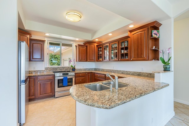 kitchen featuring light tile patterned floors, stainless steel appliances, a peninsula, a sink, and a tray ceiling