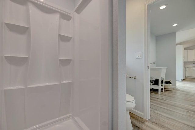 bathroom featuring baseboards, toilet, wood finished floors, walk in shower, and recessed lighting