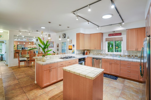 kitchen featuring a peninsula, appliances with stainless steel finishes, backsplash, tile counters, and a center island