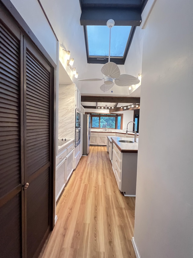 kitchen with stainless steel appliances, a sink, light wood-style floors, light countertops, and beamed ceiling