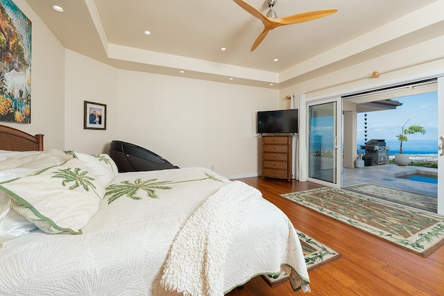 bedroom featuring recessed lighting, a raised ceiling, wood finished floors, and access to outside