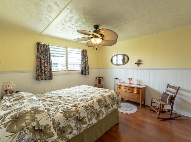 bedroom featuring a ceiling fan, a wainscoted wall, a textured ceiling, and wood finished floors