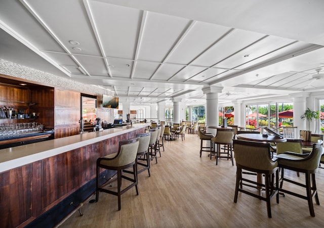 dining area featuring a community bar, light wood-type flooring, and decorative columns