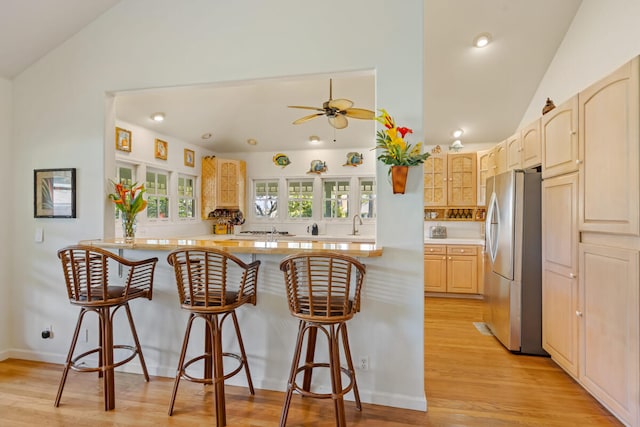 kitchen featuring stainless steel appliances, a breakfast bar, vaulted ceiling, and light wood-style flooring