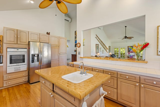 kitchen with a sink, white oven, a warming drawer, stainless steel fridge, and a center island with sink