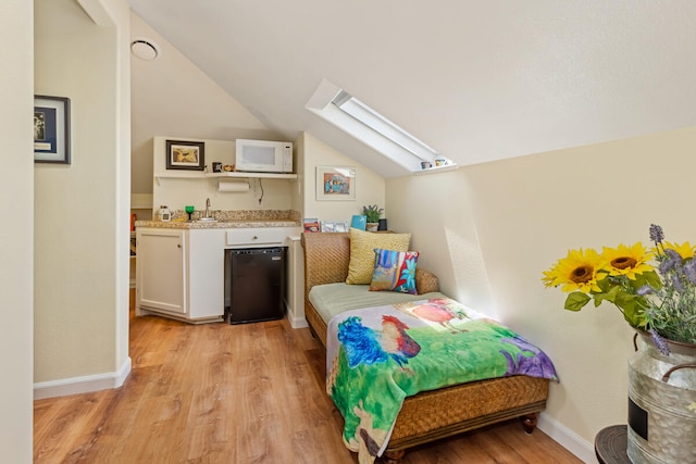 bedroom featuring light wood-style floors, vaulted ceiling with skylight, baseboards, and a sink