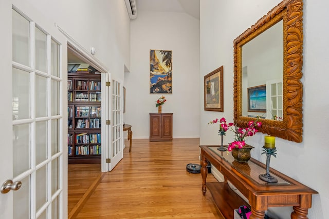 hallway featuring french doors, a towering ceiling, light wood-style flooring, and baseboards